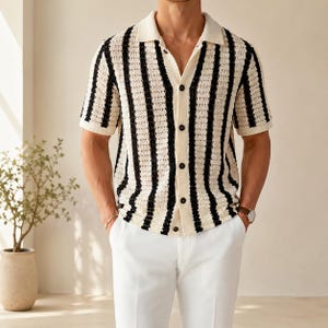 May include: A short-sleeved, button-down shirt with a cream-colored base and vertical black stripes. The shirt has a classic collar and is paired with white pants. The style is casual and suitable for warm weather.