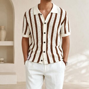 May include: A short-sleeved, button-down shirt with a cream-colored collar and vertical brown stripes. The shirt has dark buttons and is paired with white pants. The overall style is casual and suitable for warm weather.