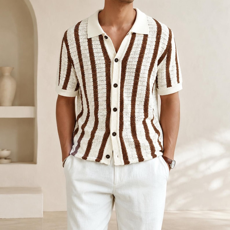 May include: A short-sleeved, button-down shirt with a cream-colored collar and vertical brown stripes. The shirt has dark buttons and is paired with white pants. The overall style is casual and suitable for warm weather.