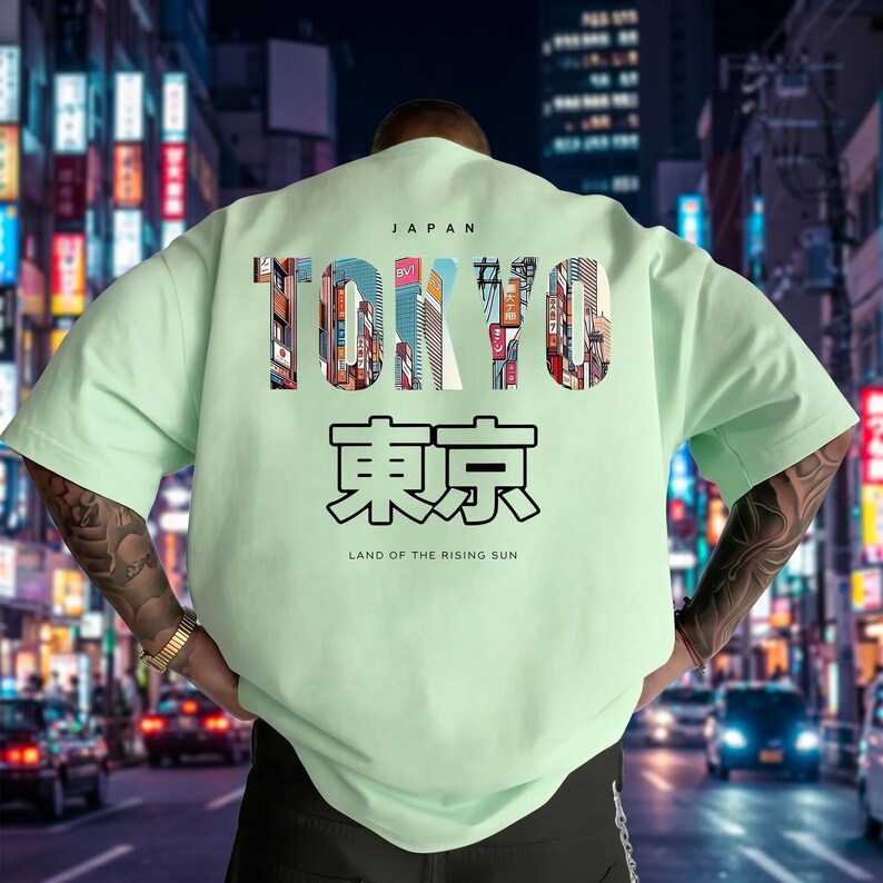 May include: A light green t-shirt with the word "TOKYO" in large, colorful letters, with the Japanese characters for Tokyo below. The shirt also includes the text "JAPAN" and "LAND OF THE RISING SUN". The design features a cityscape.