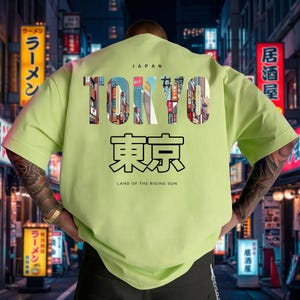 May include: A light green t-shirt with the word "TOKYO" in a colorful, cityscape design. Below, Japanese characters and the text "LAND OF THE RISING SUN" are printed. The word "JAPAN" is above the word "TOKYO".