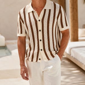 May include: A short-sleeved, button-down shirt with a cream-colored base and vertical brown stripes. The shirt has a collared neckline and is paired with white pants. The shirt's design is a knit pattern.