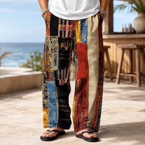 Könnte beinhalten: Weit geschnittene Hose mit Patchwork-Design aus vertikalen Bahnen in Rot-, Blau-, Gelb- und Schwarztönen. Der Stoff zeigt verschiedene komplexe Muster und Texturen, darunter geometrische Formen und florale Motive, kombiniert mit einem weißen T-Shirt.