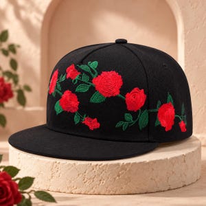 May include: A black baseball cap featuring an embroidered design of vibrant red roses with green stems and leaves. The floral pattern wraps across the front panels of the cap, which has a flat brim and a structured crown with a top button.