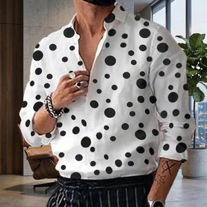 Op de afbeelding: Wit overhemd met een zwart stippenpatroon. Het shirt met lange mouwen heeft een kraag en is bovenaan opengeknoopt. Het shirt wordt gecombineerd met een zwart-wit gestreepte broek.