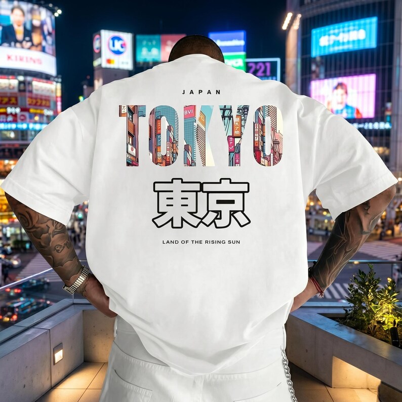 May include: White t-shirt with a graphic design featuring the word "TOKYO" in colorful letters, with Japanese characters below. The text "JAPAN" is above the word "TOKYO" and "LAND OF THE RISING SUN" is below.