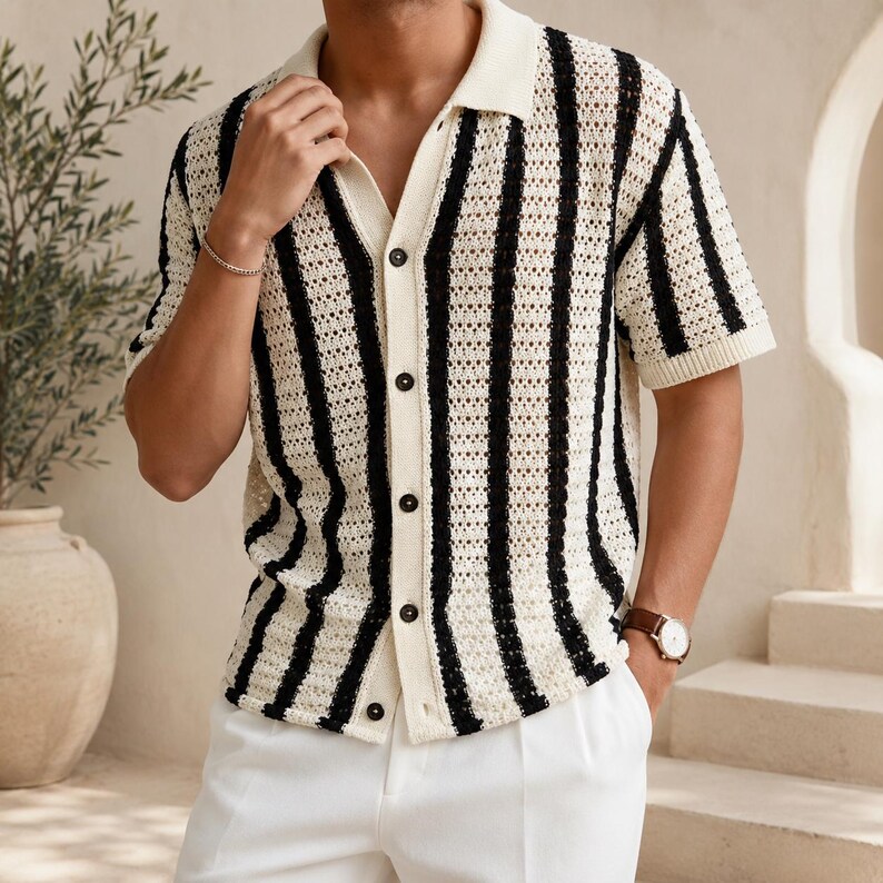 May include: A short-sleeved, button-down shirt with a cream-colored base and bold black vertical stripes. The shirt features a classic collar and is paired with white pants. The knit fabric has a textured appearance, and the shirt has dark buttons.