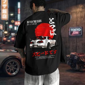 Puede incluir: Camiseta negra con un gráfico de un coche deportivo blanco, un sol rojo y texto japonés. La camiseta presenta las frases "OUTRUN THE CLOCK" y "TOKYO JDM". El gráfico del coche incluye el texto "Throttle to the horizon, carve every curve with fire."