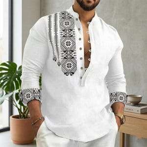 May include: White long-sleeve shirt with a mandarin collar and a button-down front. The shirt features a black and white geometric pattern on the upper left chest and cuffs. The shirt is made of a lightweight fabric.