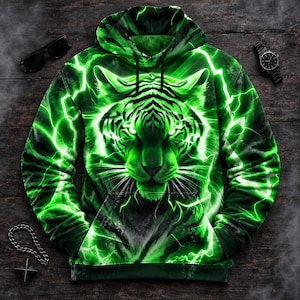 Pode incluir: Uma camisola com capuz e mangas compridas com uma estampa gráfica vibrante de um rosto de tigre rodeado por relâmpagos verde-brilhantes. O capuz inclui um cordão, punhos canelados, bainha canelada e um bolso frontal tipo canguru.