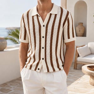 May include: A short-sleeved, button-down shirt with vertical brown and cream stripes. The shirt has a collared neckline and is paired with white pants. The buttons are dark brown. The shirt is made of a textured knit fabric.