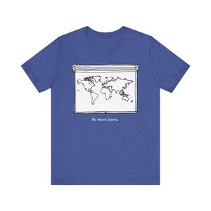 Puede incluir: Camiseta azul con un diseño de mapa del mundo en blanco y negro dentro de una bolsa con cremallera. El texto "We were here" está impreso debajo del gráfico. La camiseta es de material suave.