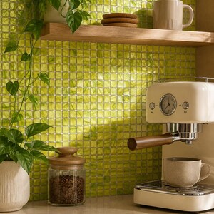 May include: A kitchen scene featuring a light green square tile backsplash, a wooden floating shelf with a beige mug and small wooden coasters, a potted green plant, a glass jar with a wooden lid containing coffee beans, and an espresso machine.