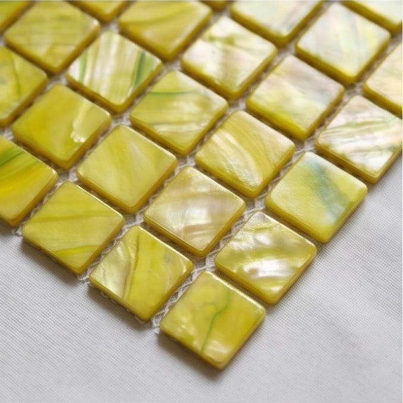 May include: A grid of square, yellow glass tiles featuring a smooth, glossy finish with subtle, swirling white and light green marbled patterns throughout each individual piece, arranged in a uniform pattern on a white mesh backing.