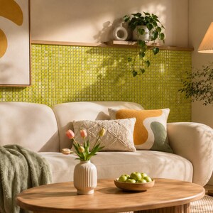 May include: A cream-colored sofa with a green throw blanket, two decorative pillows, and a wooden coffee table. On the table sits a white ribbed vase with pink tulips and a wooden bowl filled with green apples. A floor lamp stands to the right.