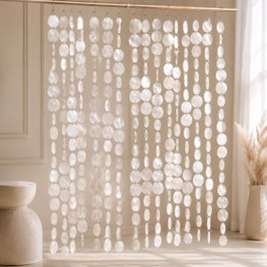 May include: A hanging room divider curtain composed of multiple vertical strands of circular, iridescent white shell discs. Each strand is suspended from a horizontal metal rod, featuring varying sizes of reflective, flat, round shell pieces.
