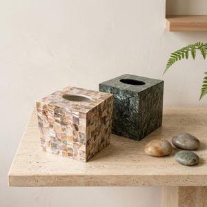 May include: Two square tissue box covers with an oval opening at the top. One cover features a mosaic of iridescent, light-colored mother-of-pearl tiles, while the other is crafted from dark, deep green, textured shell tiles in a mosaic pattern.