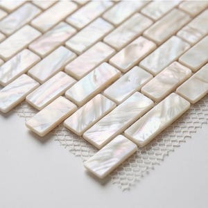 Könnte beinhalten: Nahaufnahme einer Mosaikfliesenplatte mit rechteckigen, irisierenden Perlmuttfliesen. Die Fliesen sind in einem Ziegelmuster angeordnet, mit einer weißen Netzrückseite. Die Fliesen haben einen perlmuttartigen Glanz, der das Licht reflektiert.