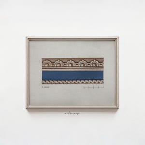 Puede incluir: Obra de arte enmarcada con un diseño arquitectónico detallado. La obra muestra una sección de moldura decorativa con detalles marrones y blancos sobre una banda azul. El marco es plateado y la obra está sobre un fondo gris claro. El texto "M. BANK" es visible.