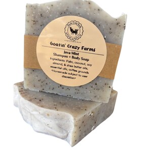 May include: Two bars of handmade Java Mint shampoo and body soap from Goatin' Crazy Farms. The soap is a light gray color with black specks and is wrapped in brown paper with a label that lists the ingredients: palm, coconut, soy almond, shea butter oils, essential oils, coffee grounds. The label also states that the soap is homemade and subject to user discretion.