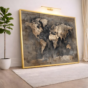May include: A large framed world map print with gold detailing. The map has a vintage, textured design with gold continents set against a dark grey background. The frame is gold, and the artwork is leaning against a white wall.