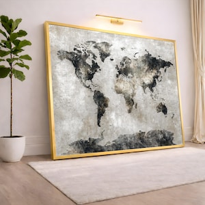 Könnte beinhalten: Ein großer gerahmter Weltkarten-Druck mit einem goldenen Rahmen. Die Karte hat ein Vintage-Design in Grau- und Brauntönen. Das Kunstwerk lehnt an einer weißen Wand, mit einer Pflanze und einem Teppich im Vordergrund.