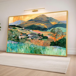 Puede incluir: Una gran impresión de arte mural rectangular en un marco dorado que representa un paisaje con montañas onduladas, un pequeño pueblo con casas blancas y un primer plano de hierba verde. La escena presenta patrones texturizados en tonos verdes, naranjas y azules.