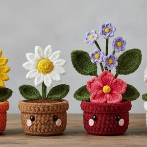 Op de afbeelding: Vier gehaakte bloempotten met lachende gezichten. De bloemen zijn onder meer een zonnebloem, een madeliefje en twee andere bloemstukken. De potten zijn oranje, bruin, rood en wit. De bloemen zijn geel, wit, roze en paars.