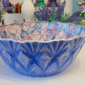 May include: A decorative blue bowl with a textured diamond pattern on the exterior. The interior features a colorful, scale-like design in shades of pink, blue, and white. The rim is accented with silver.