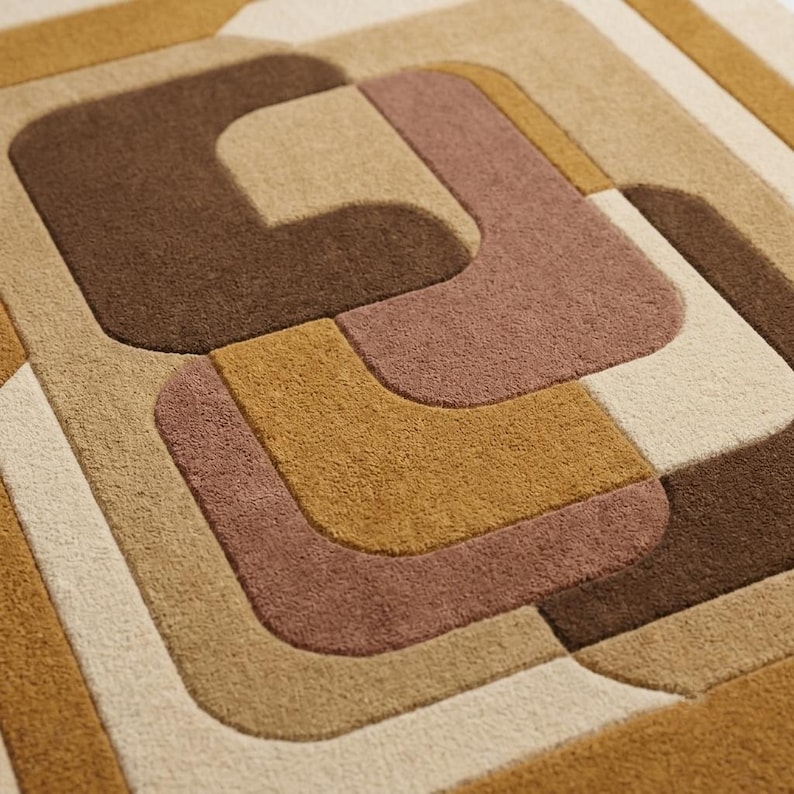 May include: A tufted area rug featuring a geometric pattern of interlocking shapes in shades of dark brown, muted mauve, golden yellow, and cream. The surface has a dense, textured pile with clearly defined edges between the colored sections.