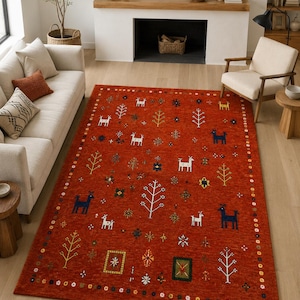 Puede incluir: Una alfombra rectangular con fondo naranja intenso que presenta un patrón repetitivo de ciervos blancos y azul oscuro, árboles estilizados y pequeños motivos florales geométricos. El borde consiste en una secuencia colorida de formas circulares.