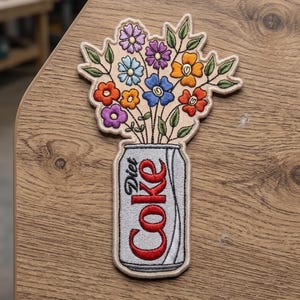 Puede incluir: Parche bordado con un ramo de flores coloridas en una lata de Coca-Cola Light. Las flores son de color púrpura, azul, naranja y rojo, con hojas verdes. La lata es plateada con texto rojo.