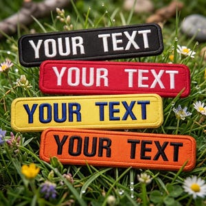 Könnte beinhalten: Vier rechteckige, gestickte Aufnäher mit dem Text "YOUR TEXT" in Weiß, Blau und Schwarz. Die Aufnäher sind schwarz, rot, gelb und orange. Die Aufnäher werden auf einem Bett aus grünem Gras mit kleinen Blumen präsentiert.