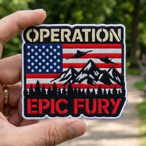 May include: A rectangular patch with the words "OPERATION EPIC FURY" in white and red lettering. The patch features an American flag design, mountains, and two flying silhouettes.