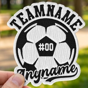 May include: A white and black embroidered patch featuring a soccer ball graphic in the center with the text #00 on the ball. The word TEAMNAME is arched across the top in black capital letters, and the word myname is written in script below.