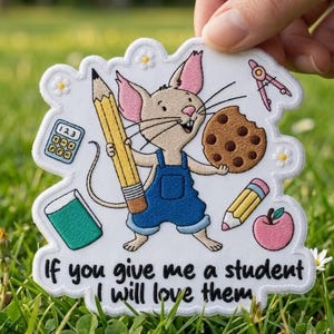 May include: A white patch featuring a cartoon mouse in blue overalls, holding a pencil and a biscuit. The patch includes a calculator, book, apple, and the text "If you give me a student I will love them."