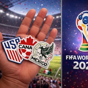 May include: A hand holding three embroidered patches with the logos of the USA, Canada, and Mexico. The background shows a soccer stadium and the FIFA World Cup 2026 logo.