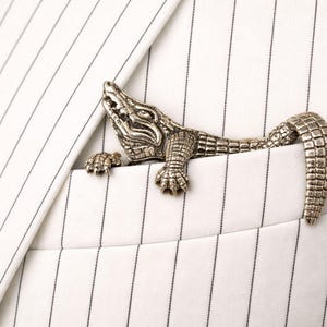 May include: A silver-colored alligator lapel pin peeking out of a white pinstripe pocket. The alligator is detailed with scales and claws, adding a touch of whimsy to the classic suit.