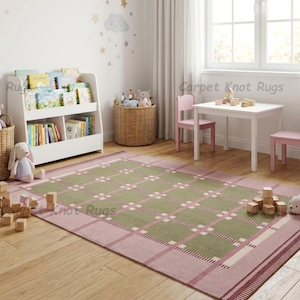 May include: A children's playroom with a pink and green plaid rug, white table and chairs, and a white bookshelf filled with books. Wicker baskets hold stuffed animals. Wooden blocks and a stuffed animal are on the floor.