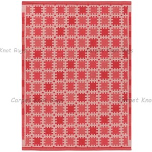 May include: A rectangular rug with a repeating geometric pattern of squares in shades of red and pink. The rug has a border and the words "Knot Rugs" and "Carpet Knot Rugs" are visible.