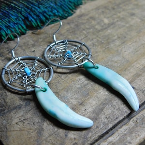 May include: A pair of silver earrings with a turquoise stone and a wire web design. The earrings are attached to a blue and white tooth-shaped charm.