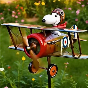 May include: A whimsical metal biplane garden stake featuring Snoopy as the pilot. The plane has a red nose, brown wings, and a spinning propeller. Snoopy wears a brown aviator helmet and red scarf. The plane has a blue and white target design on the side.