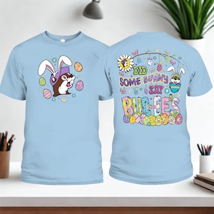 May include: Light blue t-shirts with Easter-themed graphics. One shirt features a cartoon otter wearing bunny ears and sunglasses, surrounded by Easter eggs. The other shirt says "Did Some Bunny Say Buc-ee's 2026" with Easter egg graphics.