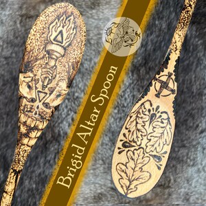 Könnte beinhalten: Hölzerner Altarlöffel mit Brandmalerei-Designs. Einer zeigt eine Fackel und einen Totenkopf, der andere Eichenblätter und ein Kreuz. Der Text "Brigid Altar Spoon" ist auf einem braunen Streifen zu sehen.