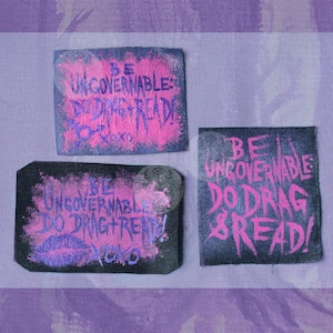 May include: Three rectangular fabric patches with black backgrounds and pink painted text. The text reads BE UNGOVERNABLE: DO DRAG + READ! XOXO. One patch features a pink lip print, while another includes a small gender symbol. The patches have raw edges.