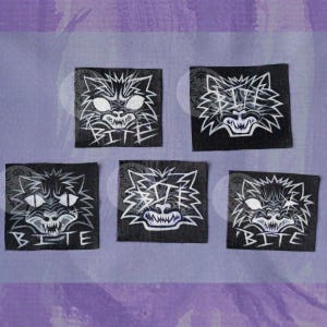 Puede incluir: Cinco parches cuadrados de tela negra con una ilustración gráfica blanca de una cara de gato estilizada con dientes afilados y la palabra BITE impresa debajo de los rasgos felinos. Cada parche muestra una variación artística diferente.