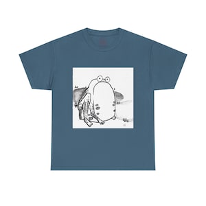 May include: A teal t-shirt featuring a black and white illustration of a cartoon frog. The frog has large eyes and is sitting on a small patch of land. The shirt is made of a soft material.