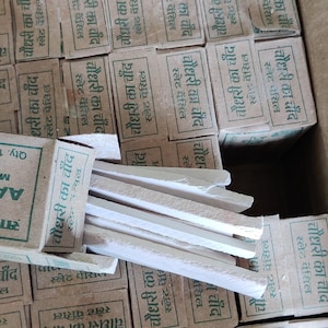May include: A box filled with small, rectangular boxes, each labelled with text in a foreign language. The boxes contain slate pencils. Some pencils are visible outside the boxes. The boxes are made of cardboard.