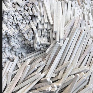 May include: A close-up image of a pile of white chalk sticks. The chalk sticks are rectangular and of varying lengths, some broken. The chalk has a slightly textured surface and is arranged in a random pile.