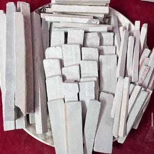 Könnte beinhalten: Eine Sammlung weißer und hellgrauer Kreidestücke in verschiedenen Formen und Größen, darunter rechteckige und quadratische, angeordnet auf einem weißen Teller. Einige Stücke sind lang und dünn, andere kurz und dick. Die Kreide hat eine leicht raue Textur.